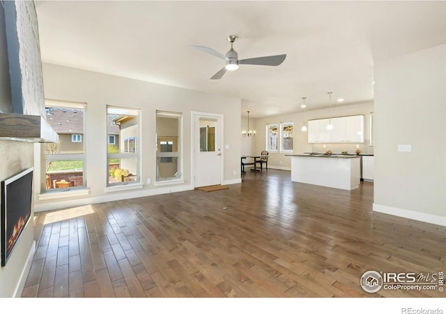 1658 Freewheel Dr, Fort Collins, CO 80525 - unfurnished living room featuring dark wood-type flooring, a warm lit fireplace, baseboards, and ceiling fan with notable chandelier