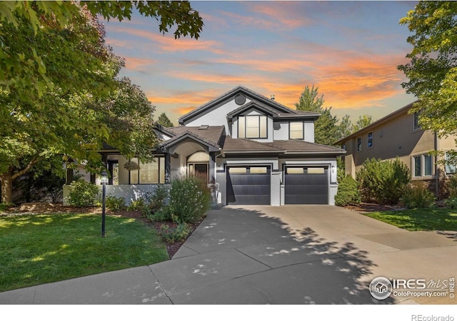 traditional home with a yard, an attached garage, a tile roof, stucco siding, and driveway