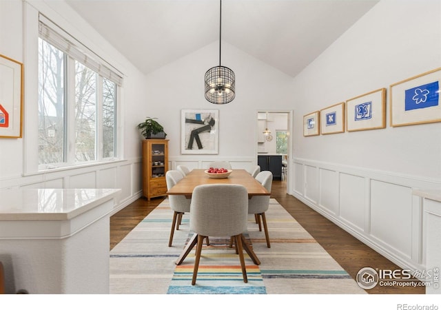 dining area with a decorative wall, dark wood-style flooring, and vaulted ceiling
