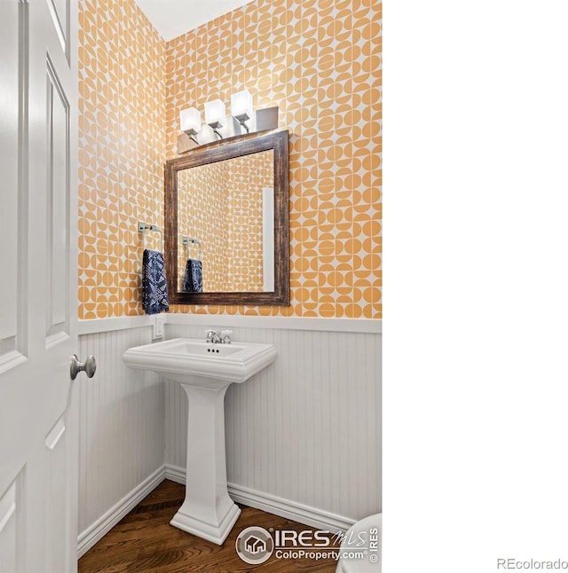 bathroom featuring wainscoting, a sink, wallpapered walls, and wood finished floors