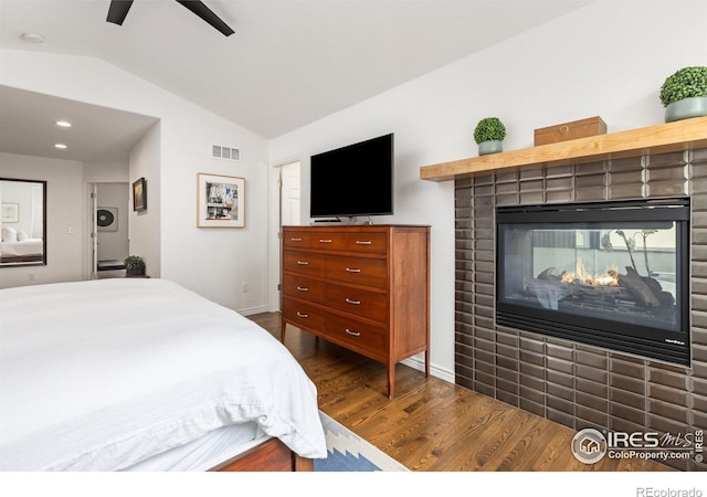 bedroom featuring dark wood-style flooring, vaulted ceiling, a multi sided fireplace, a ceiling fan, and visible vents