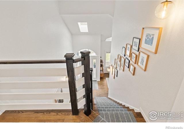 stairway with a skylight, wood finished floors, and baseboards