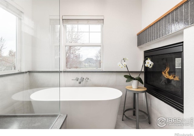 bathroom with tile patterned floors, tile walls, a freestanding tub, and a glass covered fireplace