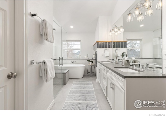 bathroom with a notable chandelier, double vanity, tile patterned floors, a freestanding bath, and a sink