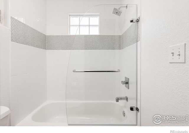 bathroom with toilet, shower / washtub combination, and a textured wall