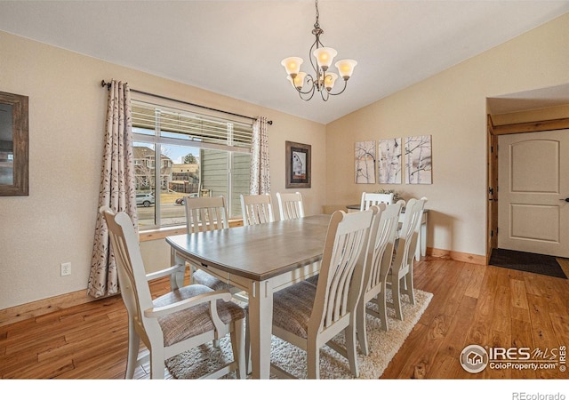 dining area with light wood-type flooring, an inviting chandelier, baseboards, and vaulted ceiling