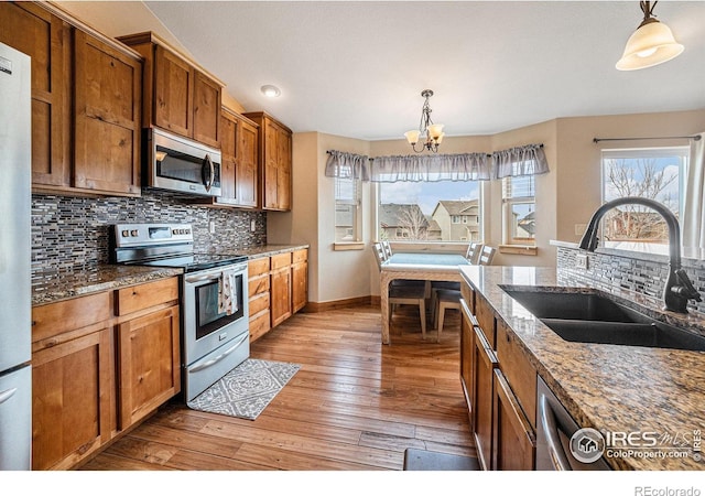 kitchen featuring an inviting chandelier, appliances with stainless steel finishes, a sink, brown cabinets, and baseboards