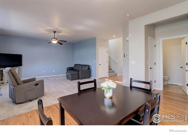 dining space featuring stairs, light wood-type flooring, baseboards, and ceiling fan