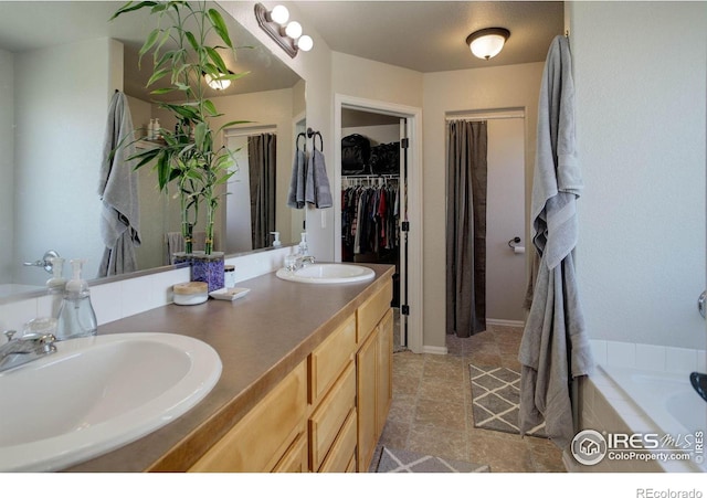 bathroom featuring a walk in closet, double vanity, tiled tub, and a sink