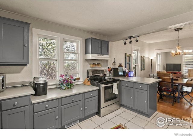 kitchen with an inviting chandelier, a peninsula, under cabinet range hood, gray cabinetry, and stainless steel electric range
