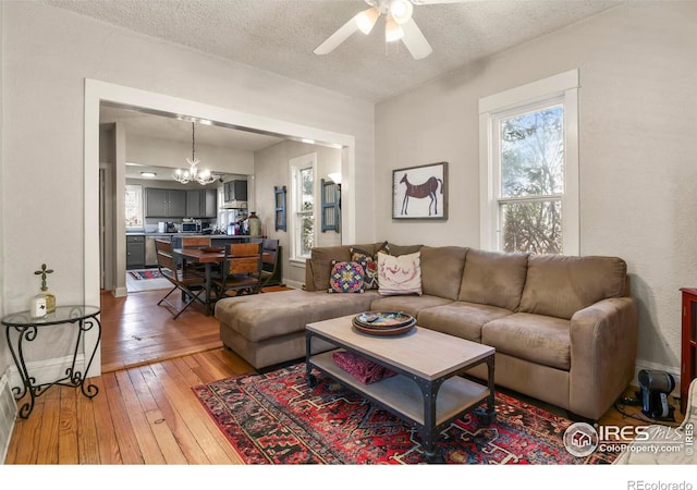 living area with light wood-style flooring, a textured ceiling, a healthy amount of sunlight, and ceiling fan with notable chandelier