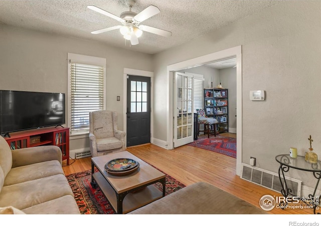 living room featuring baseboards, light wood-type flooring, a textured ceiling, and ceiling fan