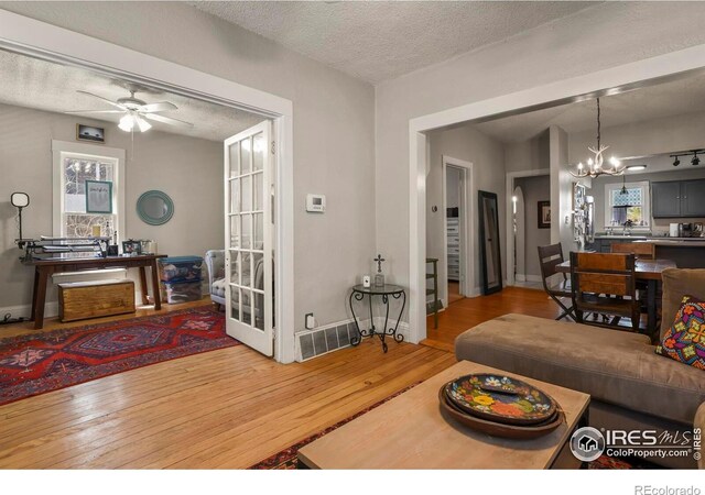 living room featuring baseboards, a textured ceiling, visible vents, wood-type flooring, and ceiling fan with notable chandelier