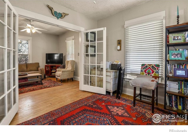 living area featuring baseboards, a ceiling fan, a textured ceiling, wood finished floors, and french doors