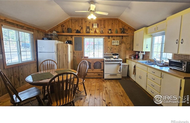 kitchen with white appliances, wood walls, a sink, lofted ceiling, and light wood finished floors
