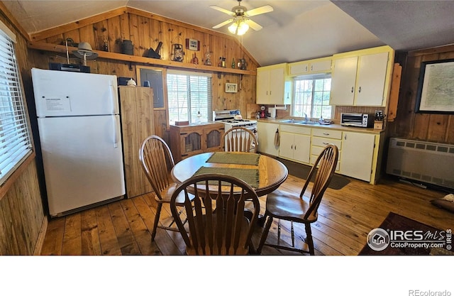 dining space with wooden walls, a ceiling fan, radiator, lofted ceiling, and wood-type flooring