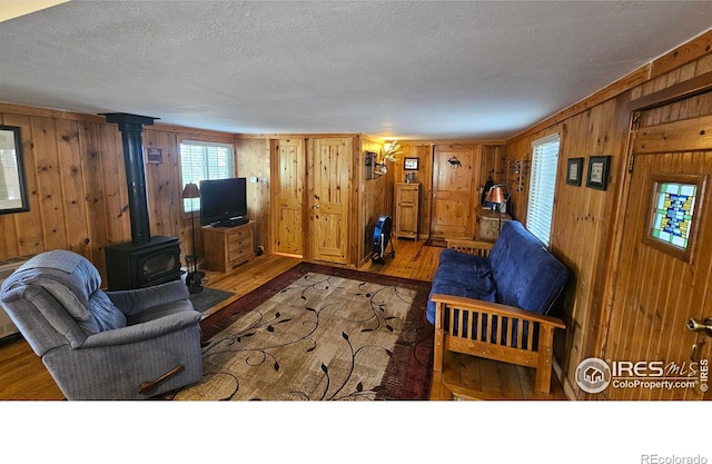 living room with wood walls, a wood stove, a textured ceiling, and wood finished floors