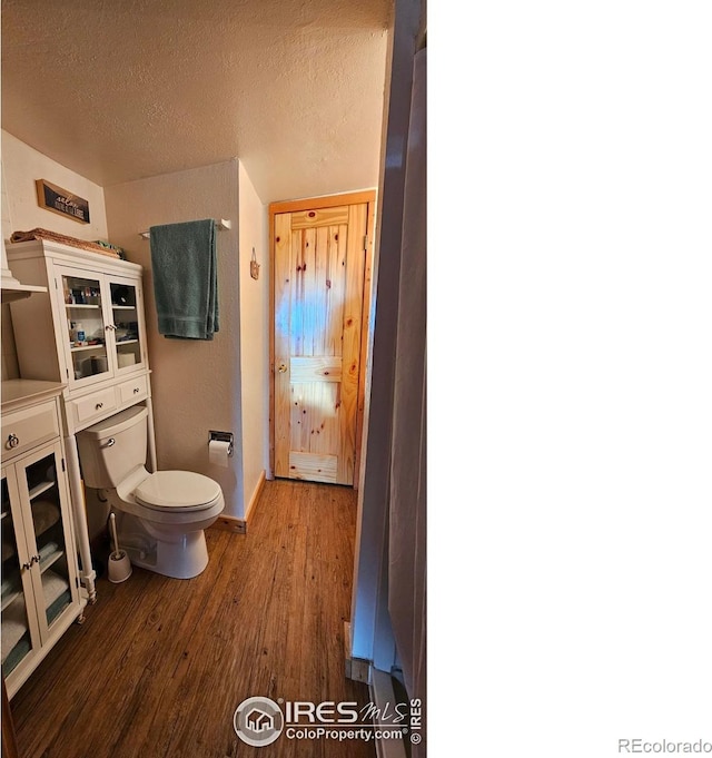 bathroom featuring toilet, baseboards, wood finished floors, and a textured ceiling