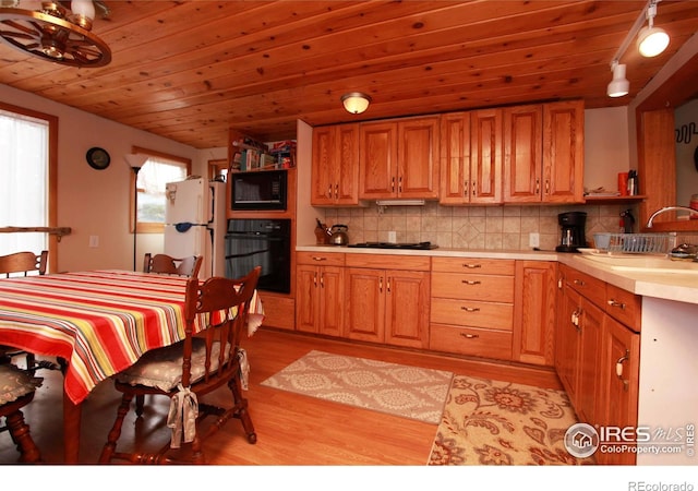 kitchen with light wood-style flooring, tasteful backsplash, black appliances, a sink, and light countertops