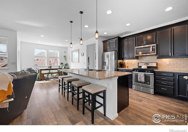 kitchen with light stone counters, a kitchen bar, appliances with stainless steel finishes, light wood finished floors, and a sink