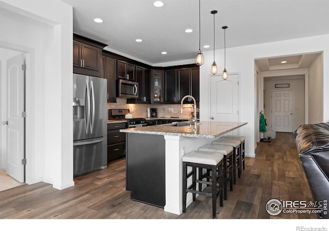 kitchen with glass insert cabinets, appliances with stainless steel finishes, a sink, a breakfast bar area, and dark wood-style floors
