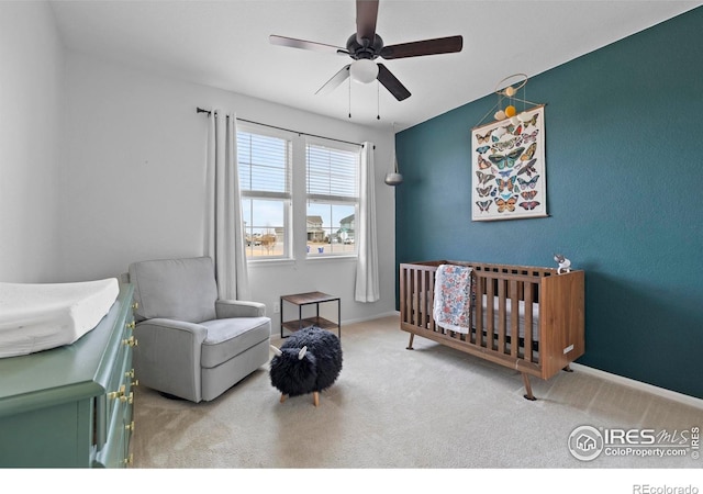 carpeted bedroom with ceiling fan, baseboards, and a crib