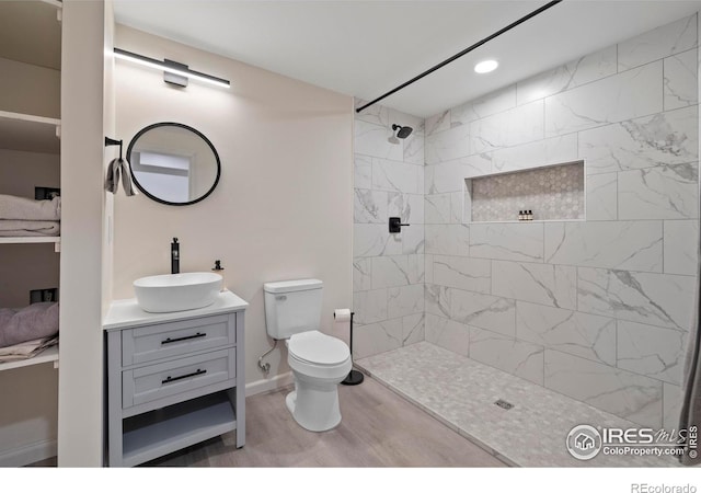 full bath featuring tiled shower, vanity, recessed lighting, toilet, and wood finished floors
