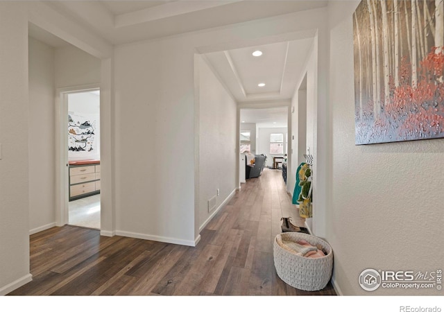 hall with visible vents, recessed lighting, wood finished floors, a raised ceiling, and baseboards