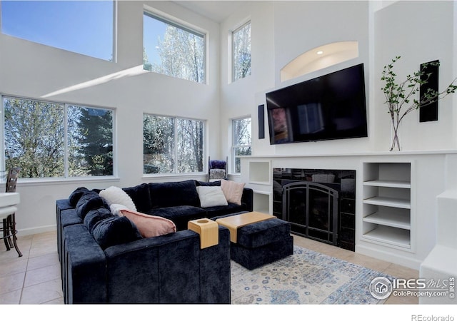 living area featuring built in features, baseboards, a towering ceiling, tile patterned floors, and a tile fireplace