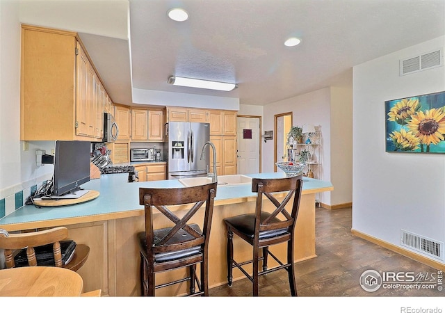 kitchen featuring visible vents, a peninsula, light brown cabinetry, and stainless steel appliances