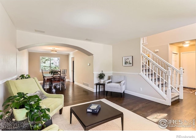 living room featuring arched walkways, visible vents, stairs, and wood finished floors