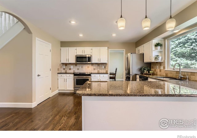 kitchen featuring white cabinets, a sink, appliances with stainless steel finishes, dark stone counters, and decorative backsplash