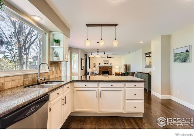 kitchen with dark stone countertops, a peninsula, dark wood-style floors, stainless steel dishwasher, and a sink