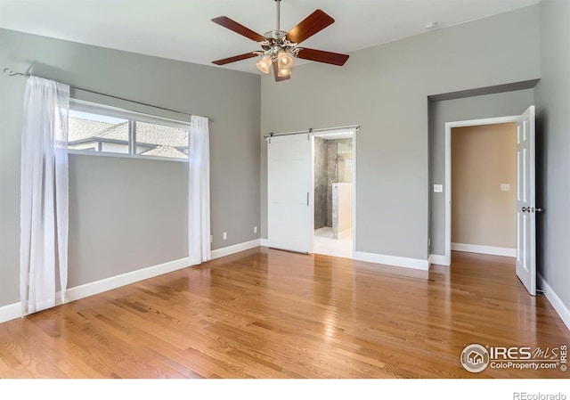 unfurnished bedroom with a barn door, baseboards, and wood finished floors