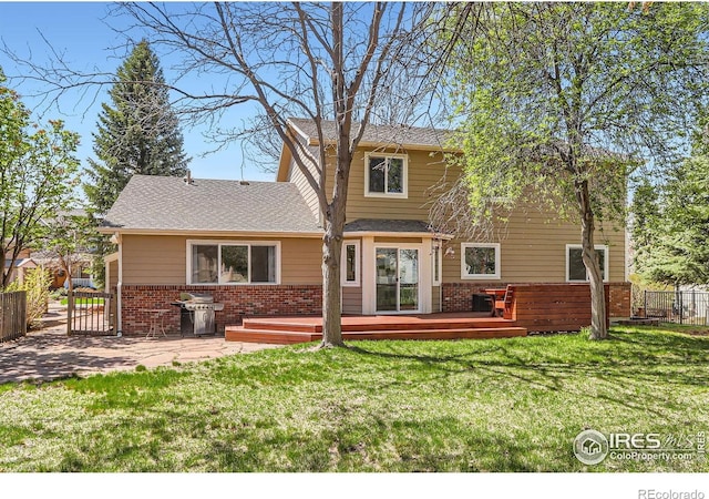 rear view of property featuring a lawn, brick siding, a wooden deck, fence, and a shingled roof