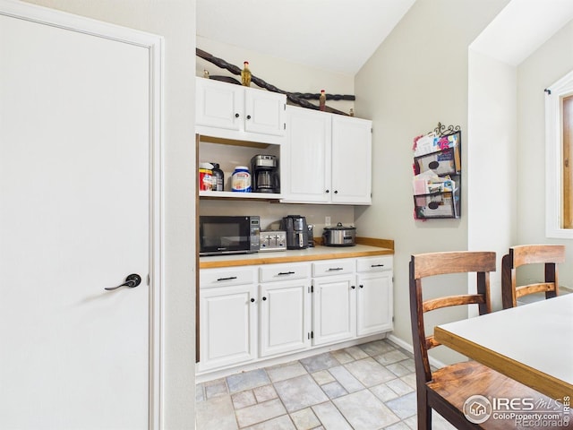 kitchen featuring baseboards, black microwave, white cabinetry, light countertops, and stone finish floor