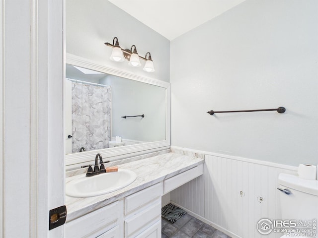 bathroom with a shower with shower curtain, vanity, wainscoting, and toilet