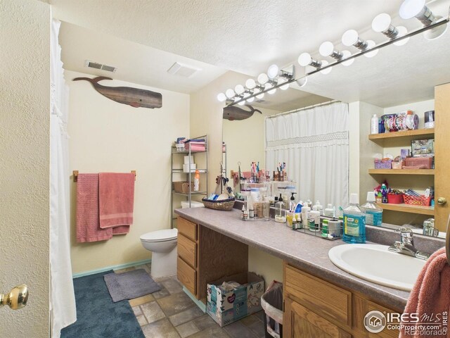 bathroom with vanity, baseboards, a textured ceiling, toilet, and visible vents