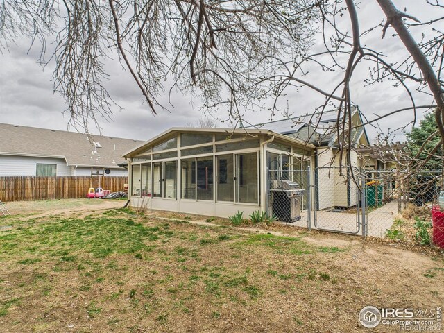 rear view of property with fence, a yard, a sunroom, and a gate