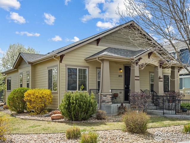 view of front of house featuring fence, covered porch, and a shingled roof