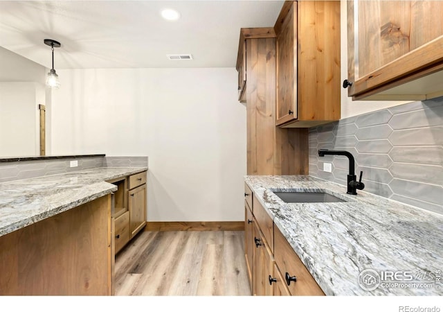 kitchen with tasteful backsplash, visible vents, a sink, light wood finished floors, and light stone countertops