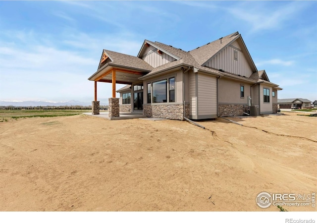 view of side of property featuring a patio, roof with shingles, stone siding, board and batten siding, and central AC unit