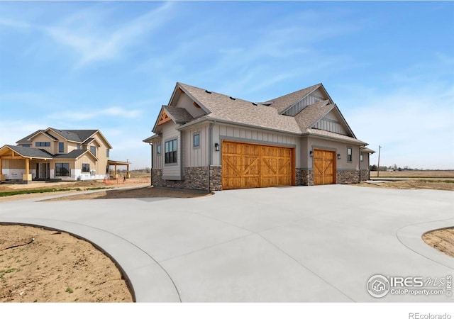 view of side of home featuring curved driveway, board and batten siding, stone siding, a garage, and a shingled roof