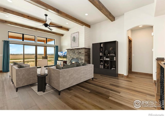 living room with wood finished floors, a ceiling fan, arched walkways, beam ceiling, and a fireplace