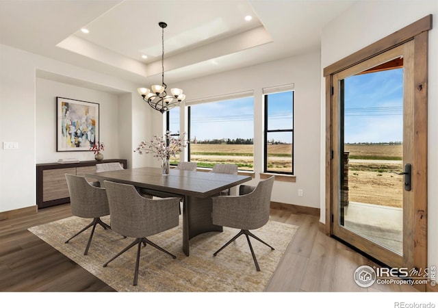 dining area featuring recessed lighting, an inviting chandelier, a tray ceiling, light wood-type flooring, and baseboards