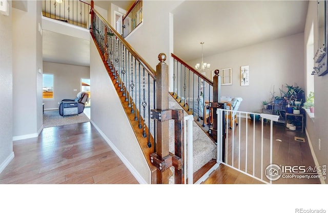 stairway with wood finished floors, a wealth of natural light, baseboards, and an inviting chandelier