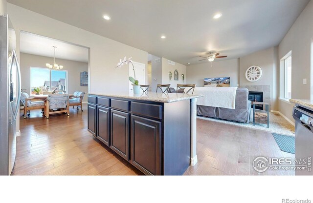 kitchen featuring ceiling fan with notable chandelier, a tile fireplace, light wood-style floors, and appliances with stainless steel finishes