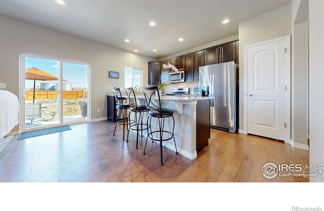 kitchen featuring a kitchen breakfast bar, light stone counters, dark brown cabinets, light wood-style floors, and appliances with stainless steel finishes