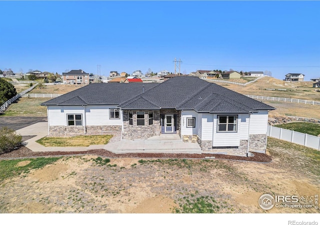 back of house featuring a fenced backyard, roof with shingles, stone siding, and a patio