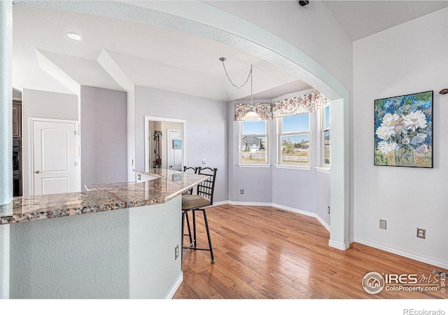 kitchen with a kitchen bar, baseboards, stone counters, and light wood-type flooring